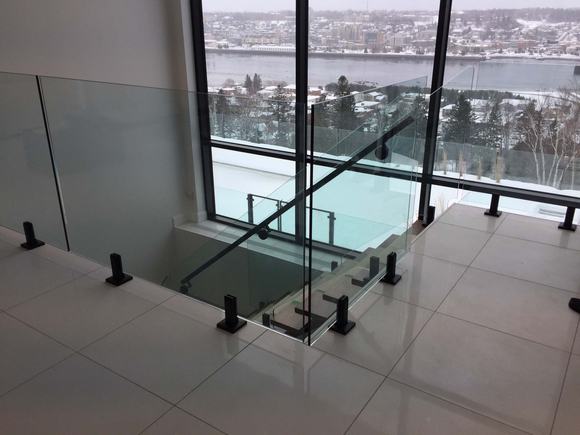 Un escalier avec une rampe en verre et une grande fenêtre.