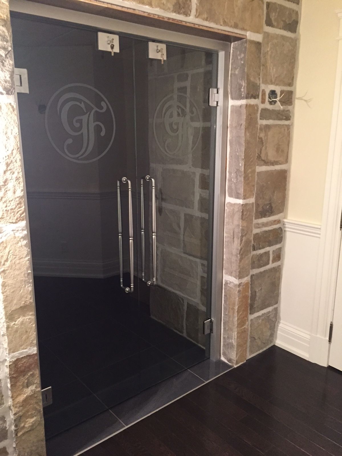 Une porte vitrée avec un monogramme dessus se trouve dans une pièce avec un mur en pierre.