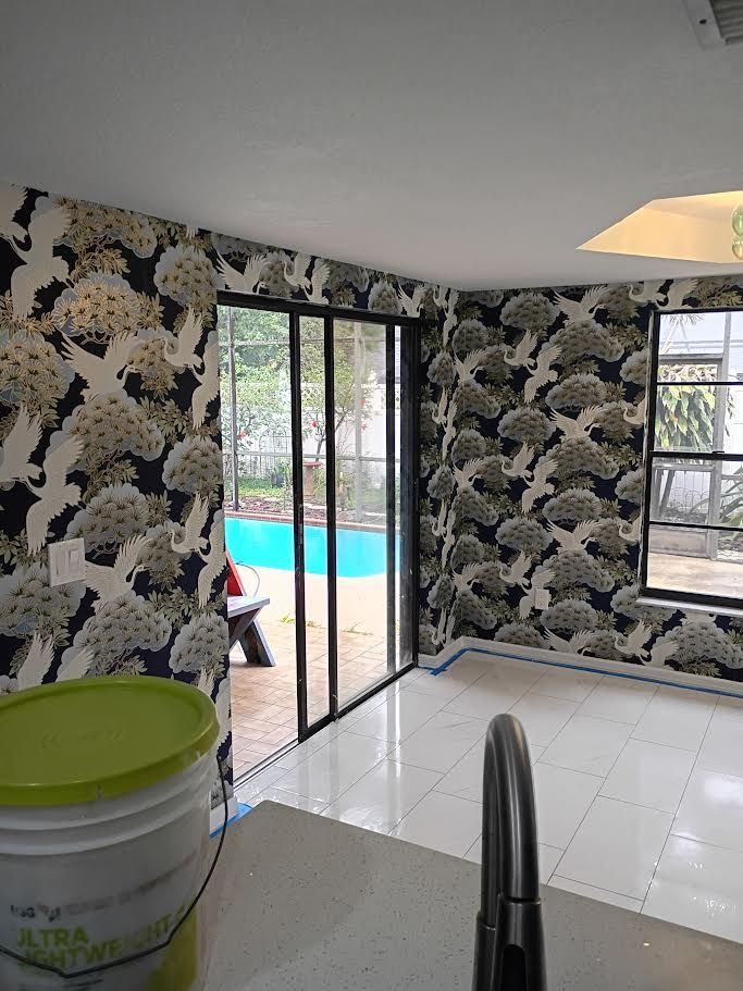 Modern room with black floral wallpaper, white tile floor, sliding glass door, and a view of a turquoise pool outside