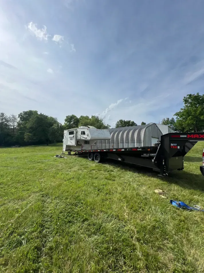 A RV is being towed by a truck in a grassy field.