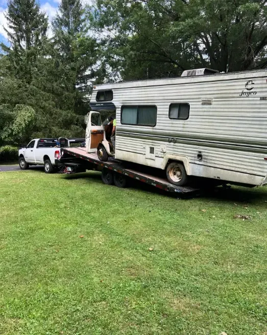 A rv is being towed by a truck on a flatbed trailer.