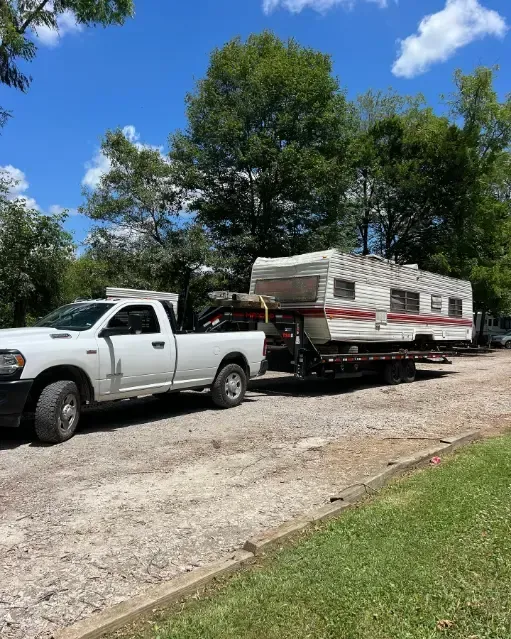 A white truck is towing a trailer down a dirt road.