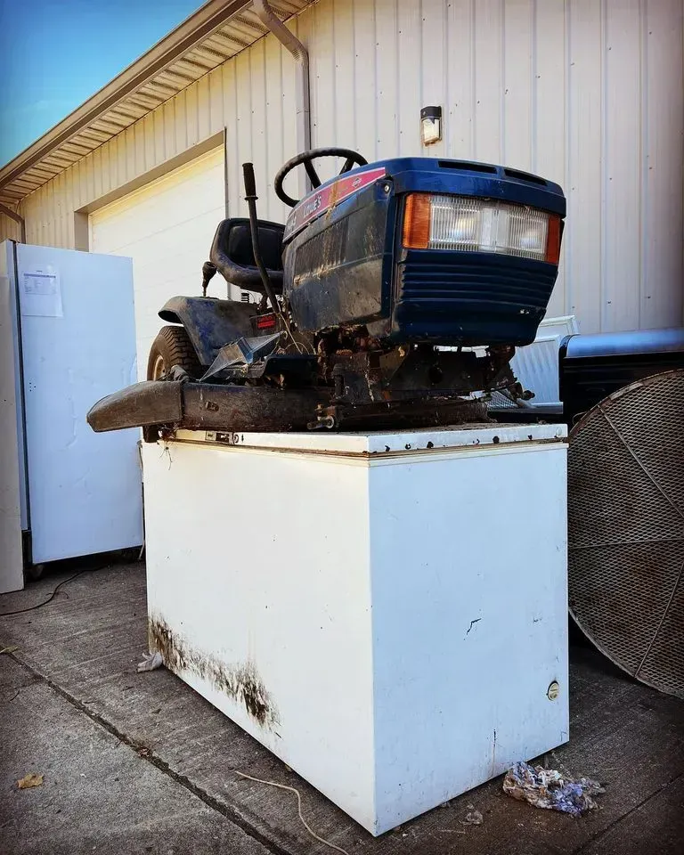 old ride-on lawnmower on top of a deep freezer, in the driveway, appliance and equipment removal services near me