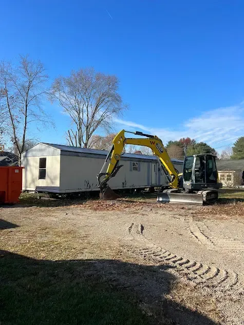 A yellow excavator is moving a trailer in a dirt lot.