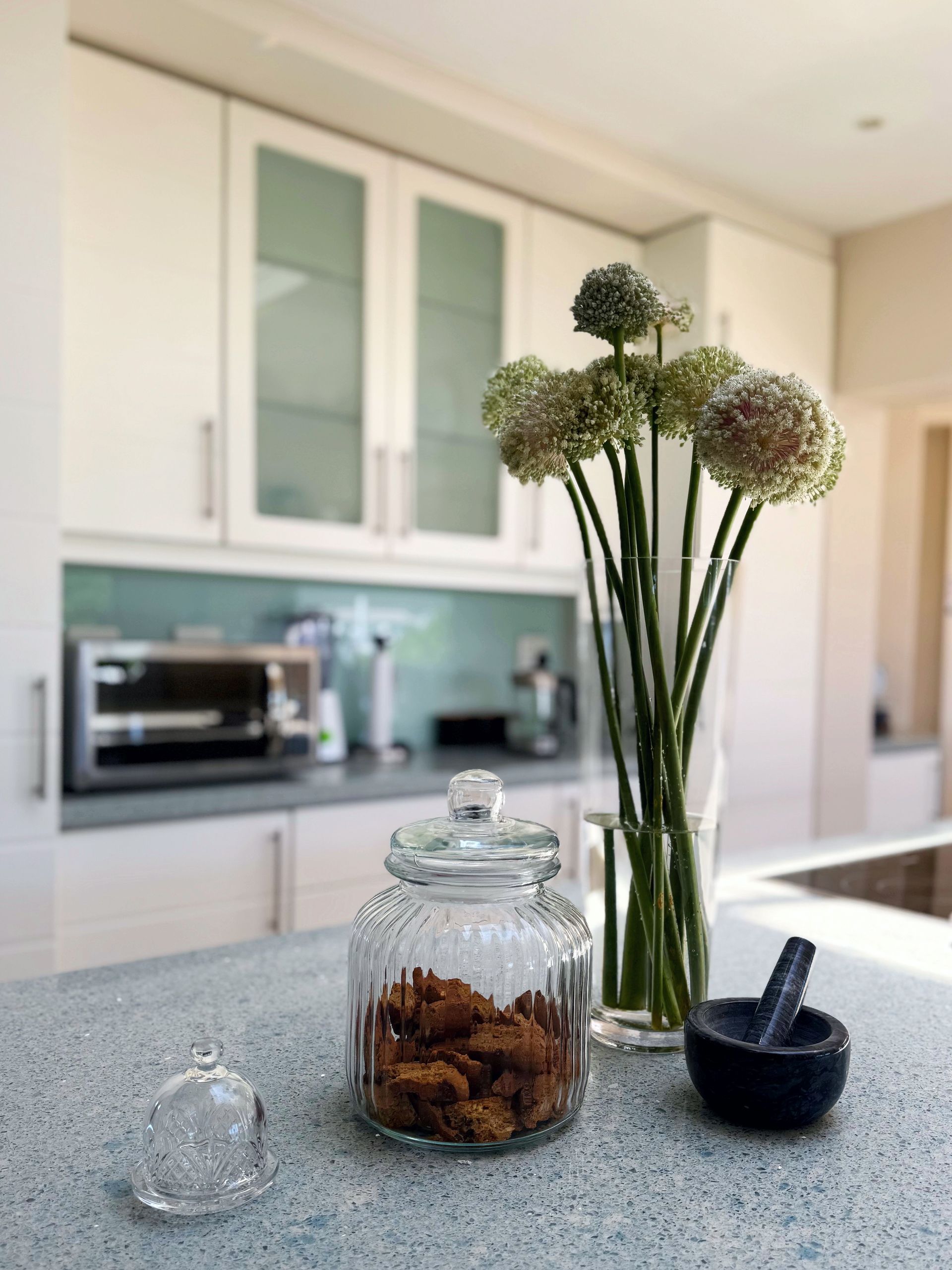 A jar of cookies sits on a counter next to a vase of flowers