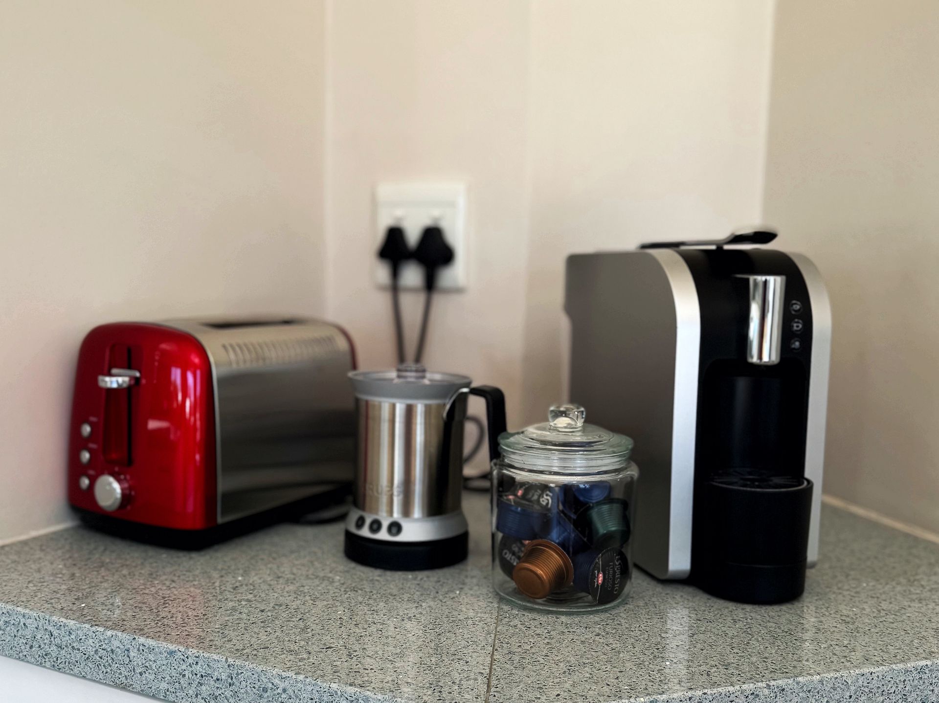 A kitchen counter with a toaster a coffee maker and a jar of coffee capsules