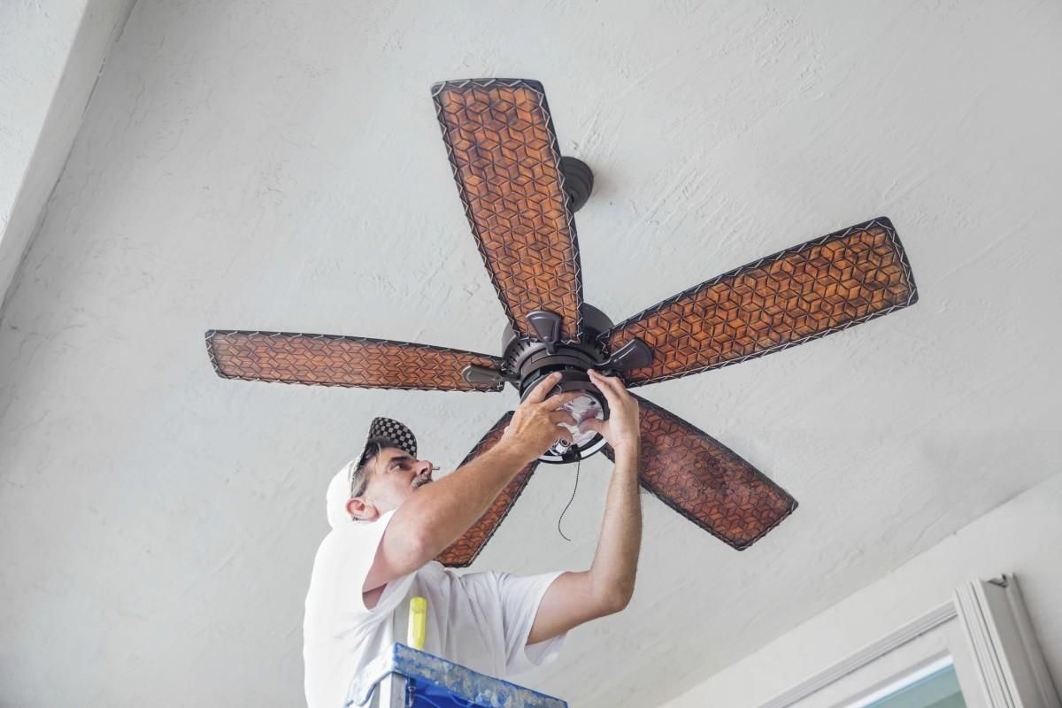 a man on a ladder fixing a ceiling fan