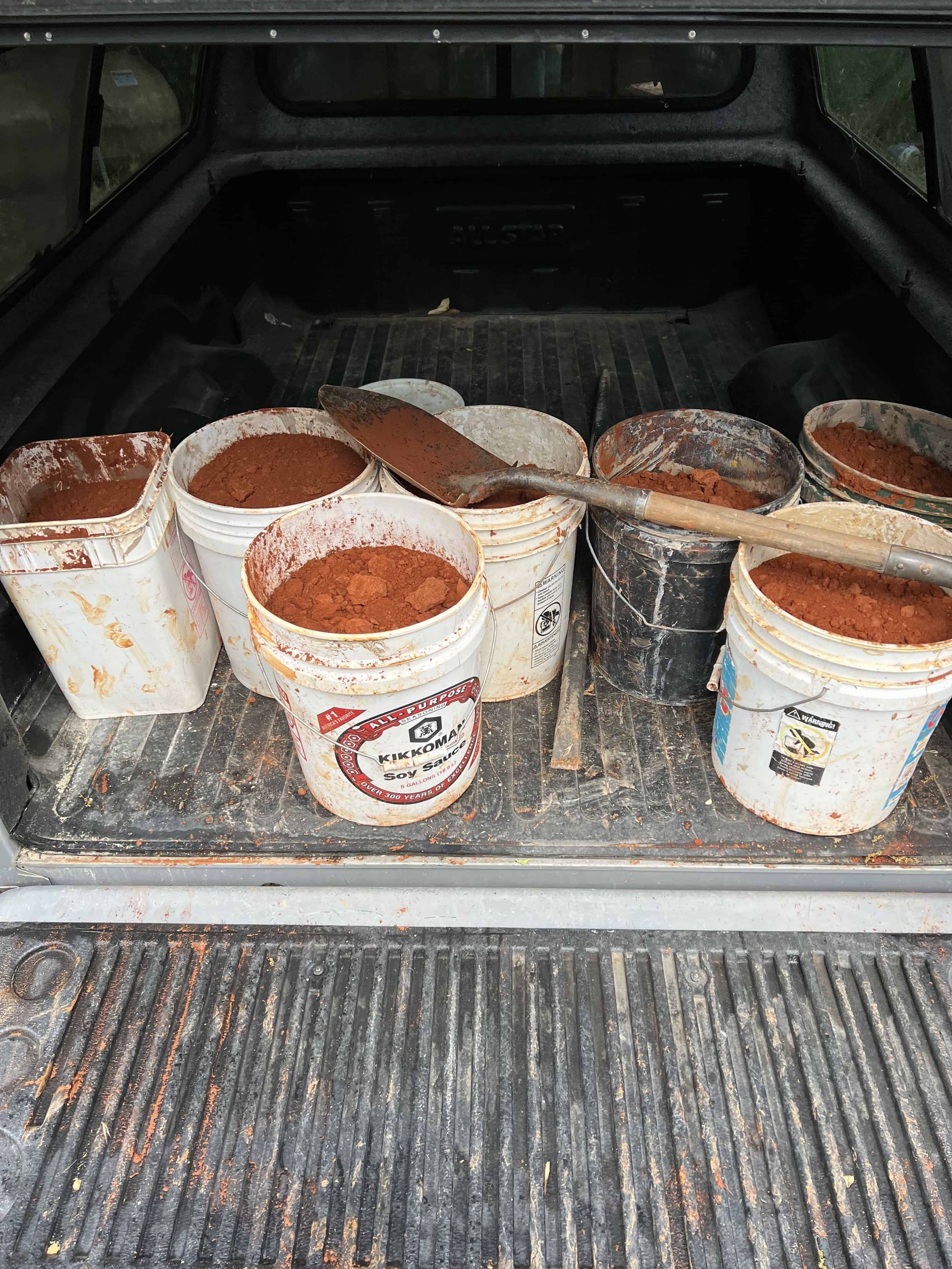 Seven buckets of red earth in the back of a truck with a shovel sitting across the top