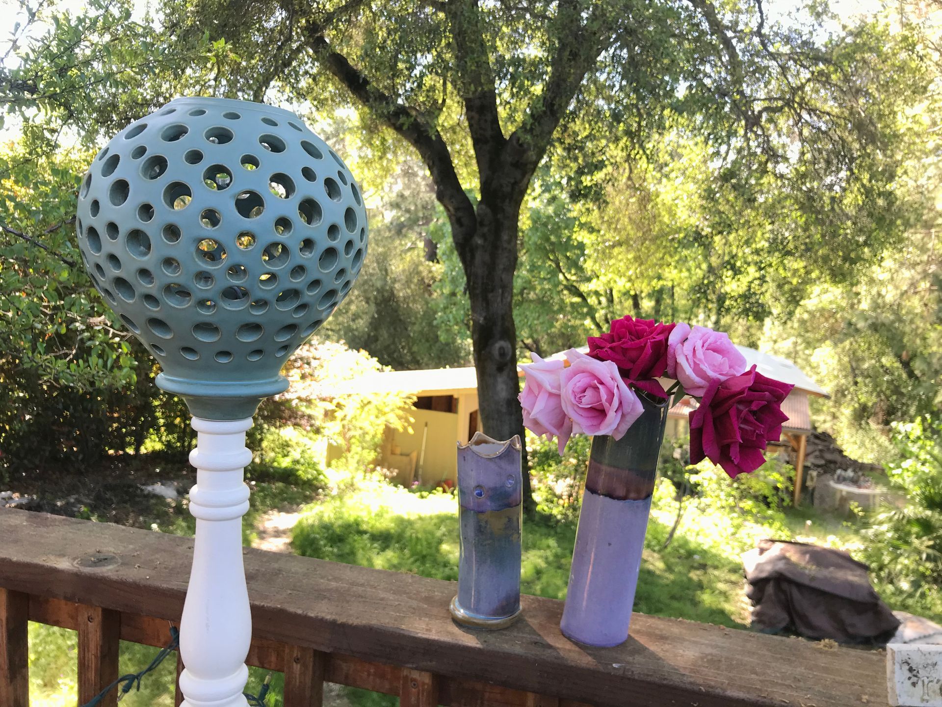 Unique round blue lamp, outside on a wooden deck with a vase of roses beside it.