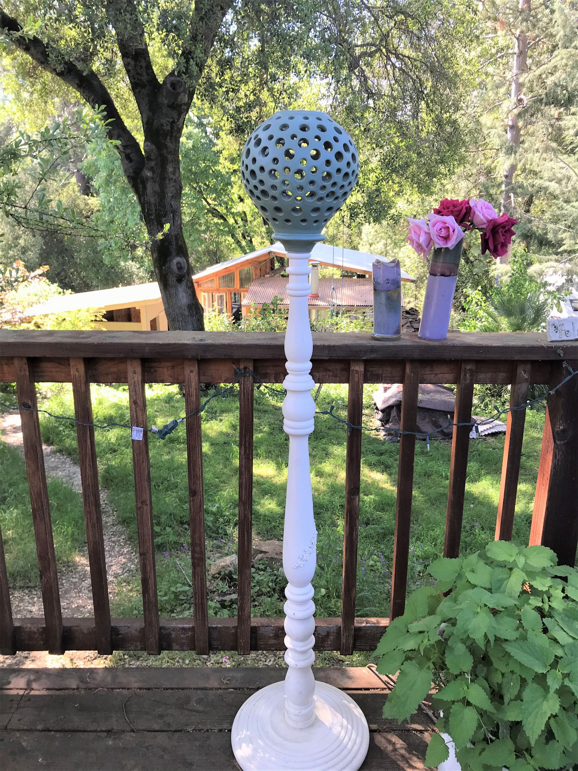 Unique round blue lamp, outside on a wooden deck with a vase of roses beside it.