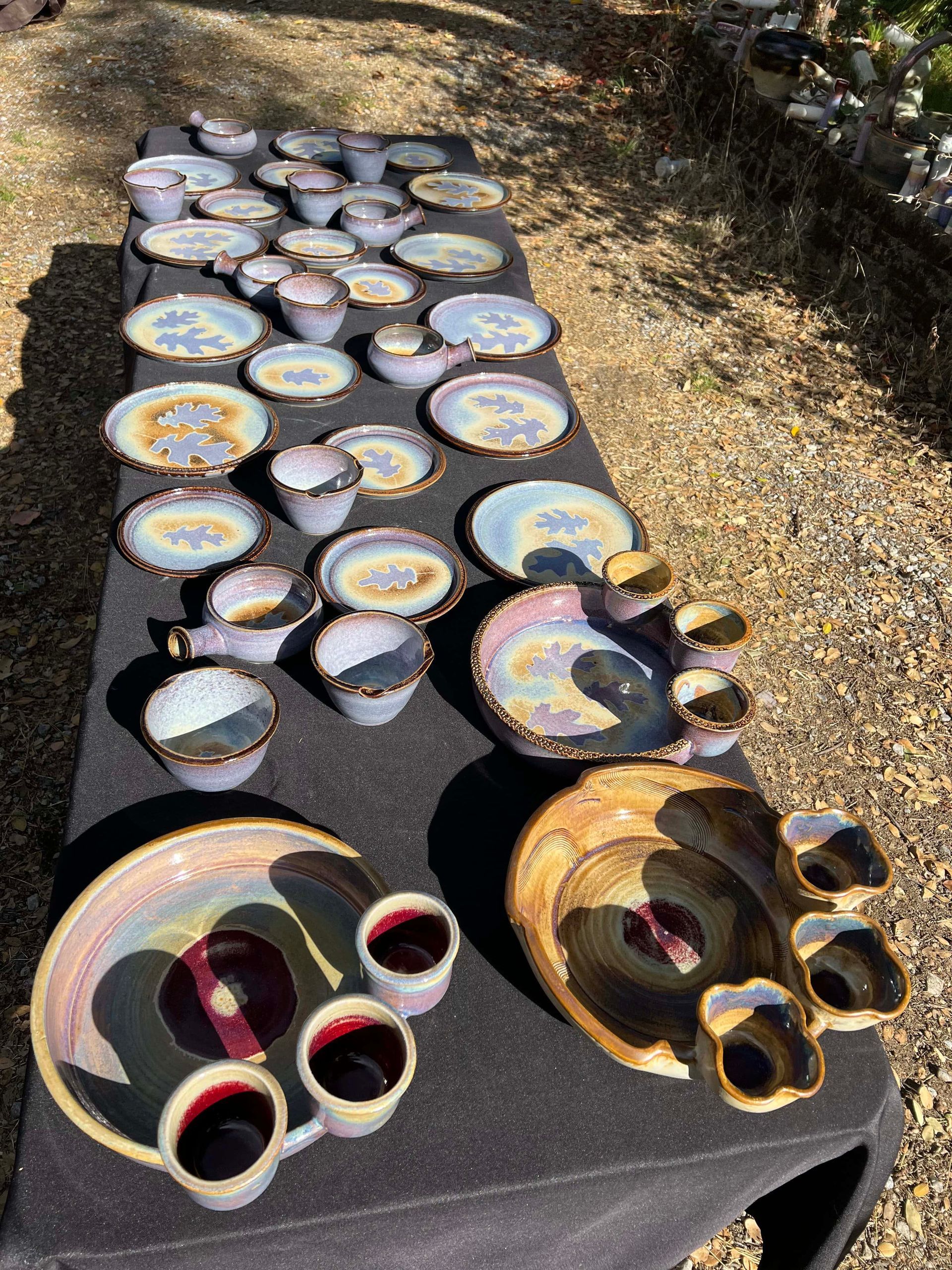 Large table covered in blue and yellow ceramic plates, bowls, and mugs, with purple oak leaf silhouettes in center