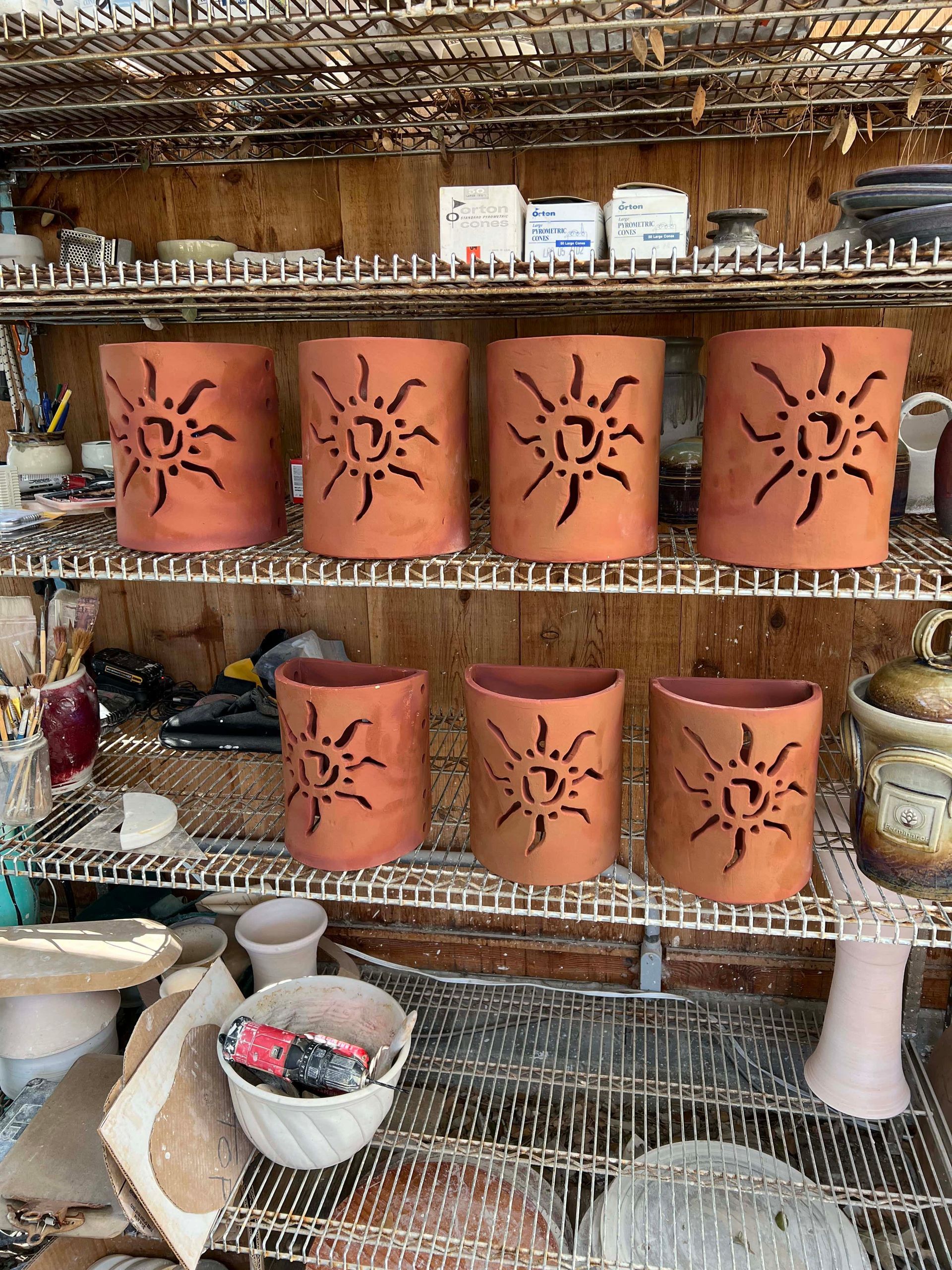 Seven clay containers with suns carved into the middle of each sitting on two stacked shelves