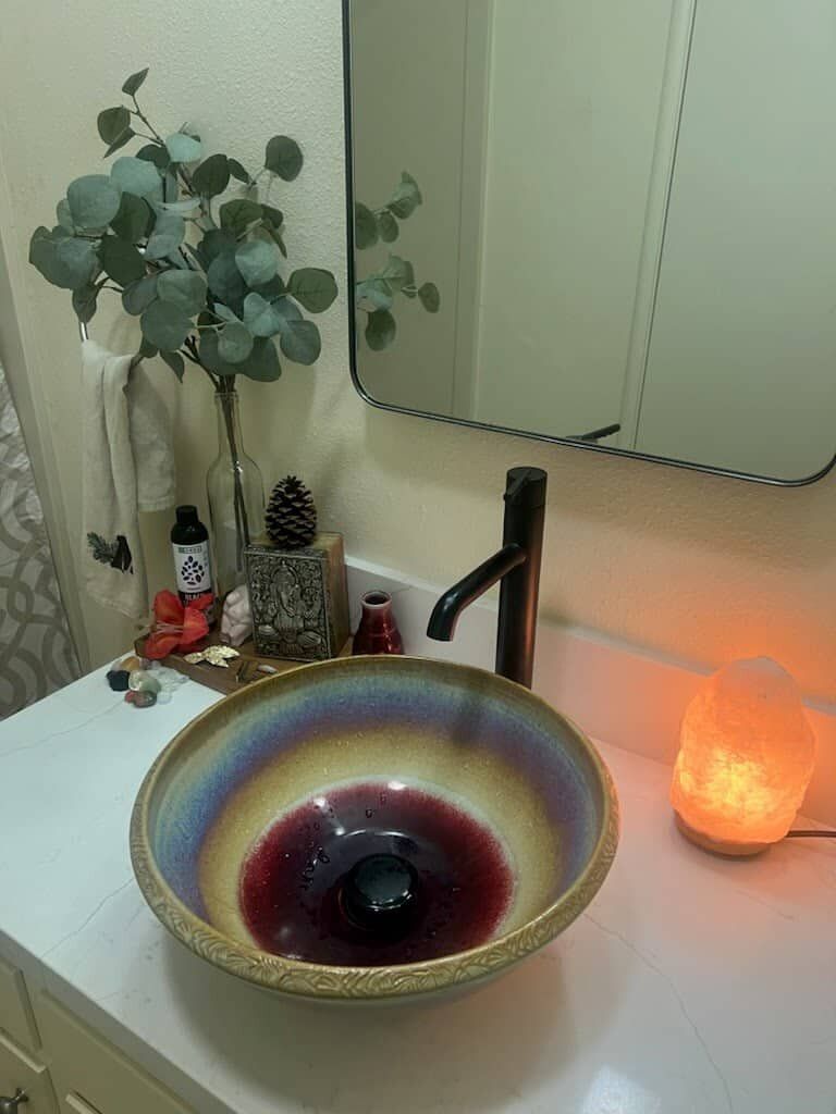 A colorful ceramic bathroom sink on a white countertop with a salt lamp beside it.