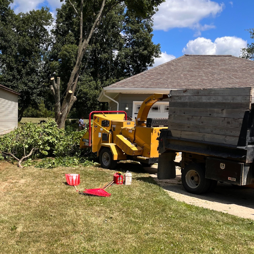 A yellow tree chipper is parked in front of a house.