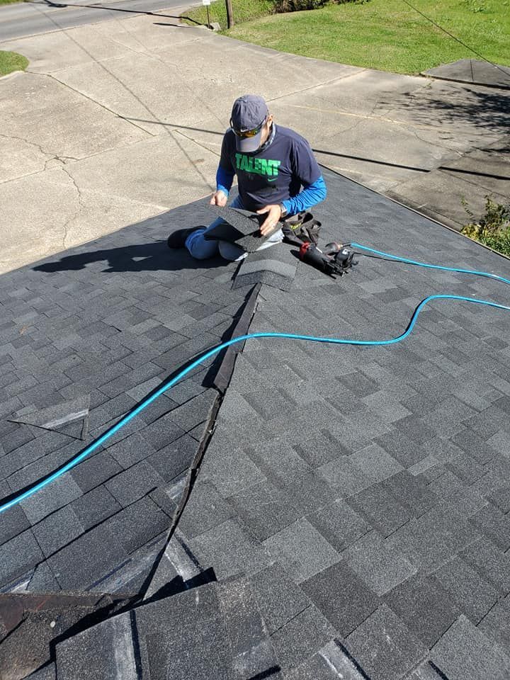 Person on a roof, installing shingles. Gray and black roof, blue hose, sunny day.