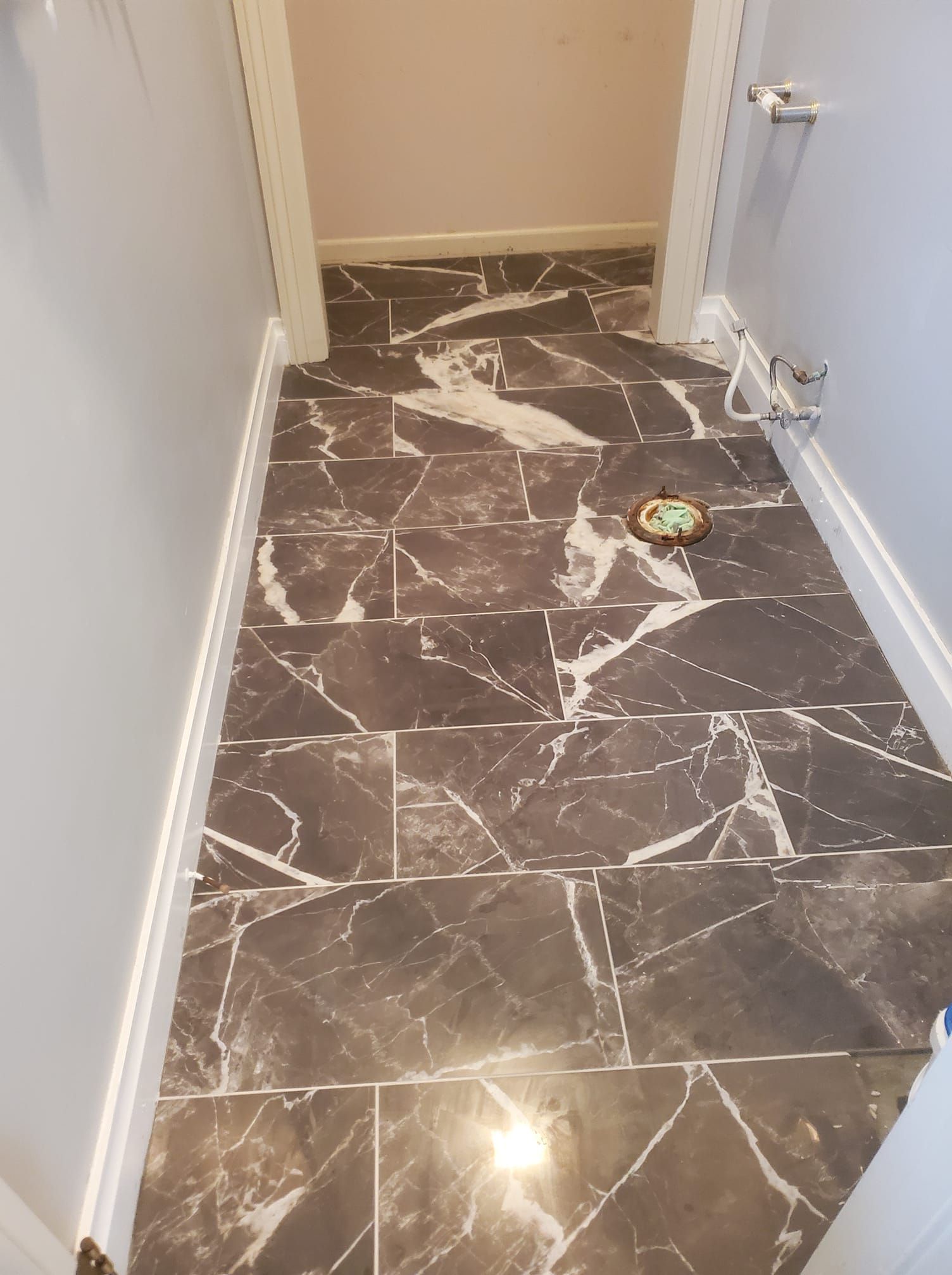 Dark gray marble-look tiled floor in a narrow hallway, leading to a room with light pink walls.