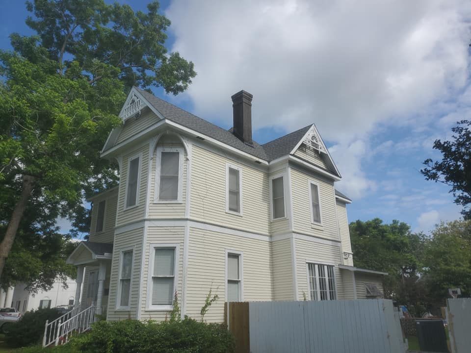 Cream-colored two-story house with black chimney, white trim, and a gray roof; set against a cloudy blue sky.