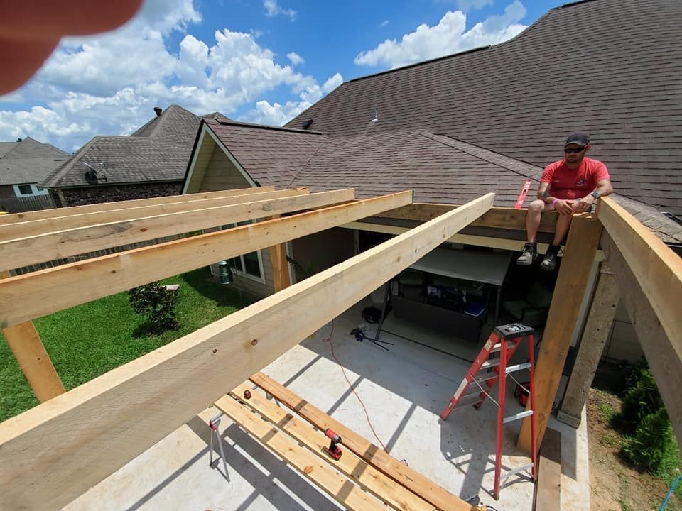 Man sitting on unfinished pergola roof; backyard setting with house.