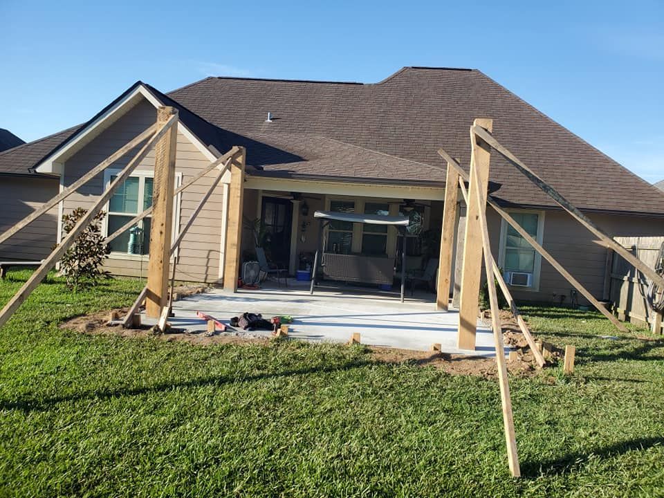 Concrete patio construction. Wooden posts with bracing. House in background, grassy yard.