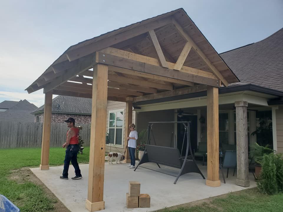 A wooden patio cover attached to a house. Two people and a dog are present.