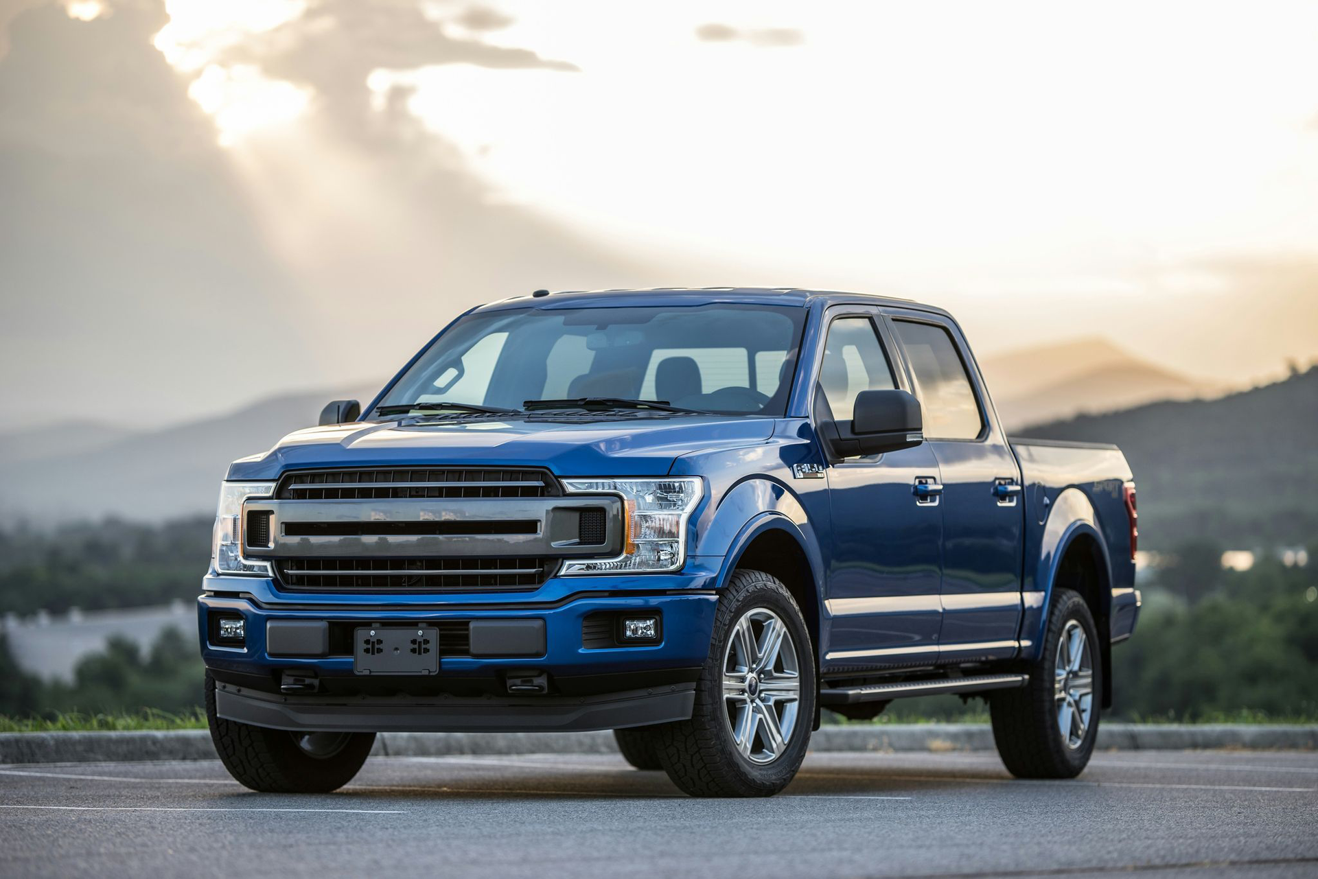 Blue pickup truck on a road with mountains and sunset in the background