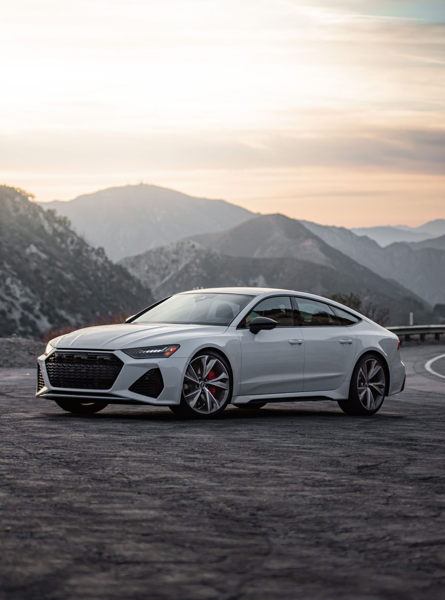 Silver sports coupe parked on a mountain road at sunset with hills in the background