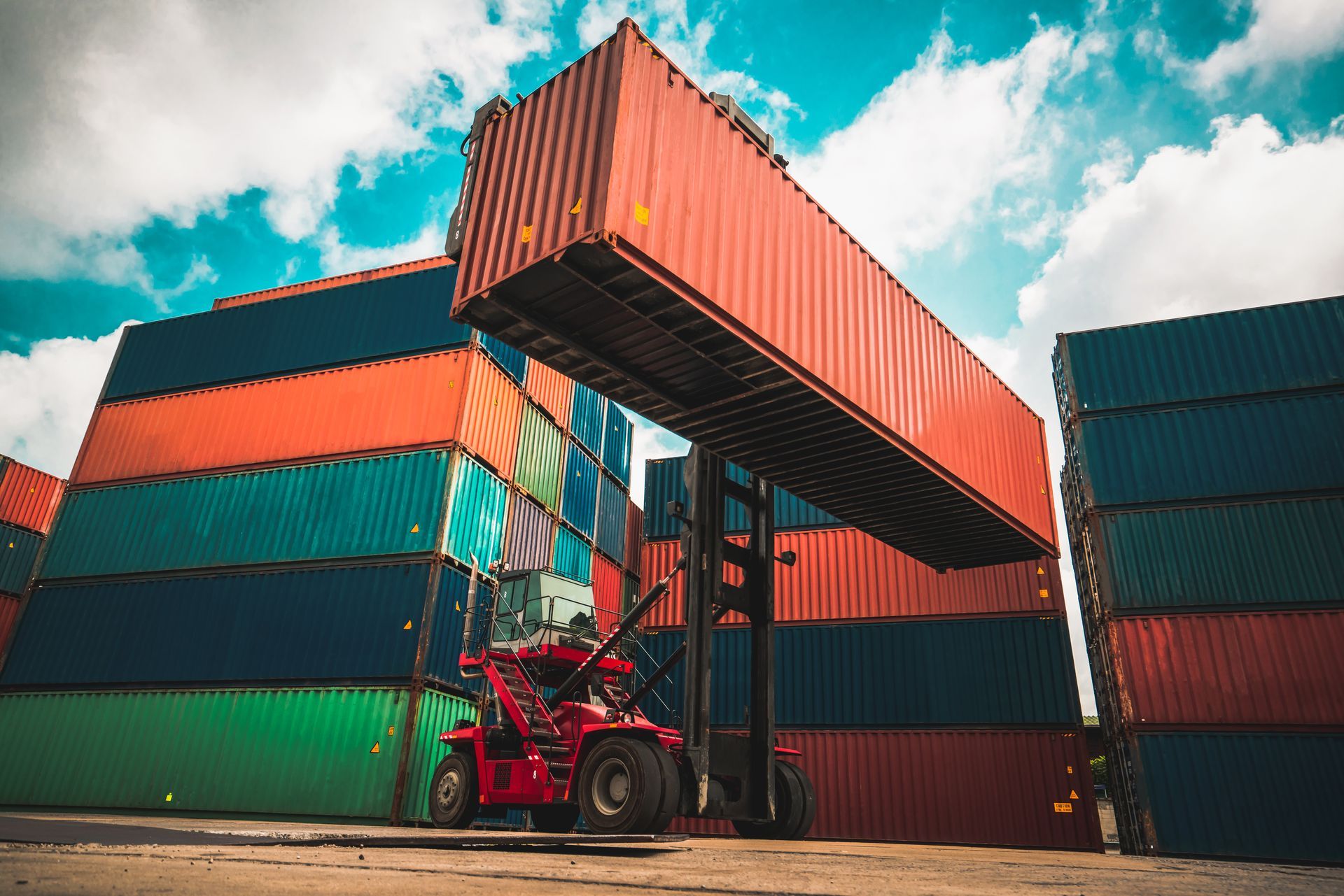 Local container supplier stacking cargo containers with forklift at industrial storage yard.