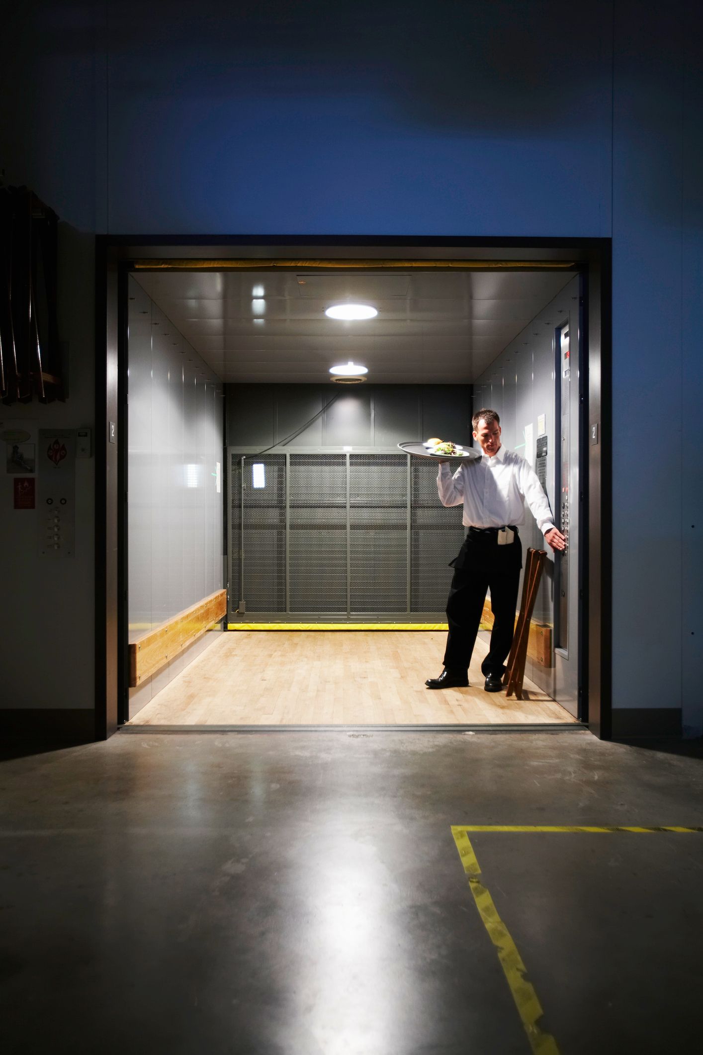 Male waiter holds a food tray as he knocks on the door of a storage container.