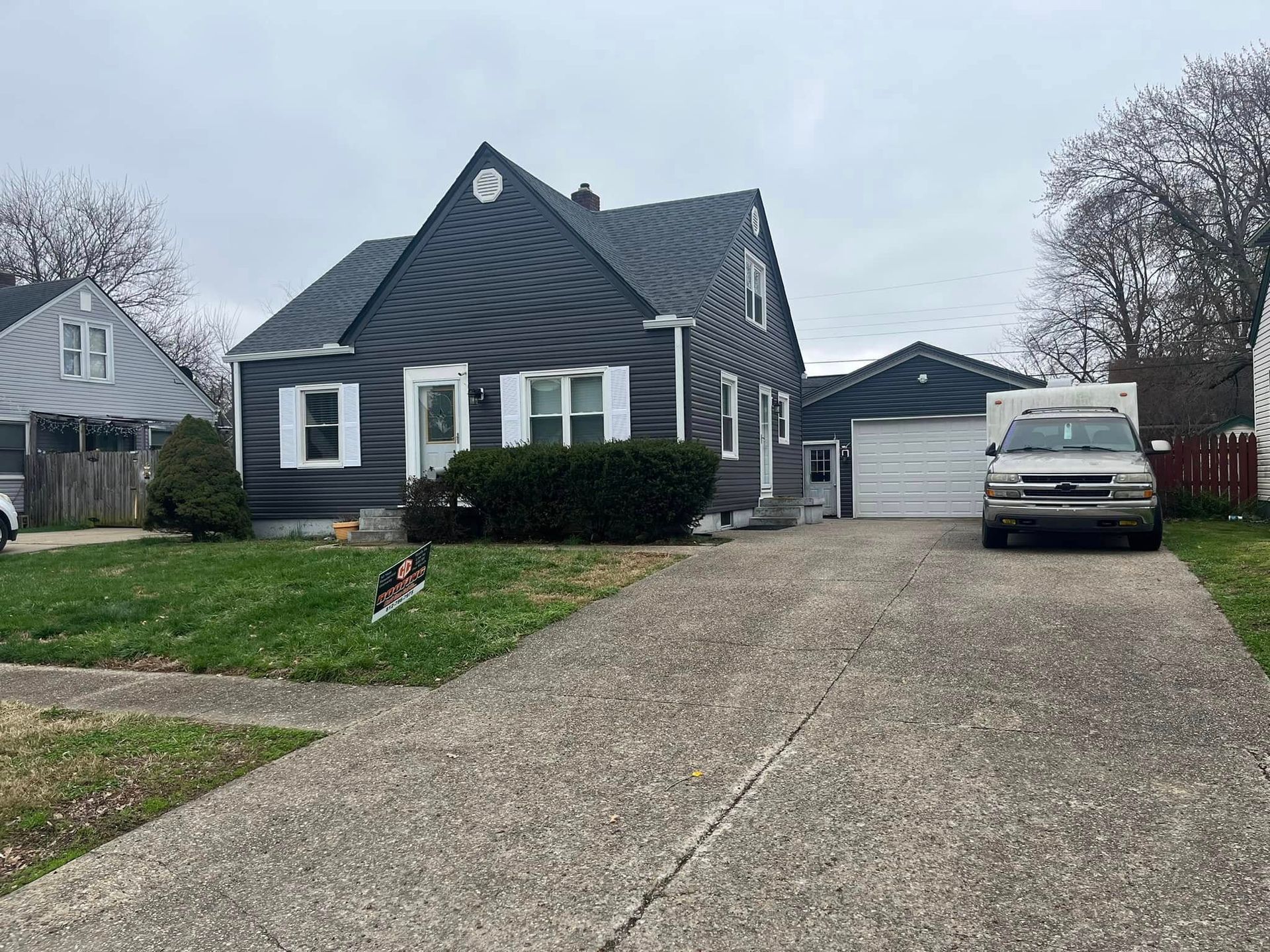 A dark gray house with white trim, a concrete driveway, and a parked SUV on a cloudy day.