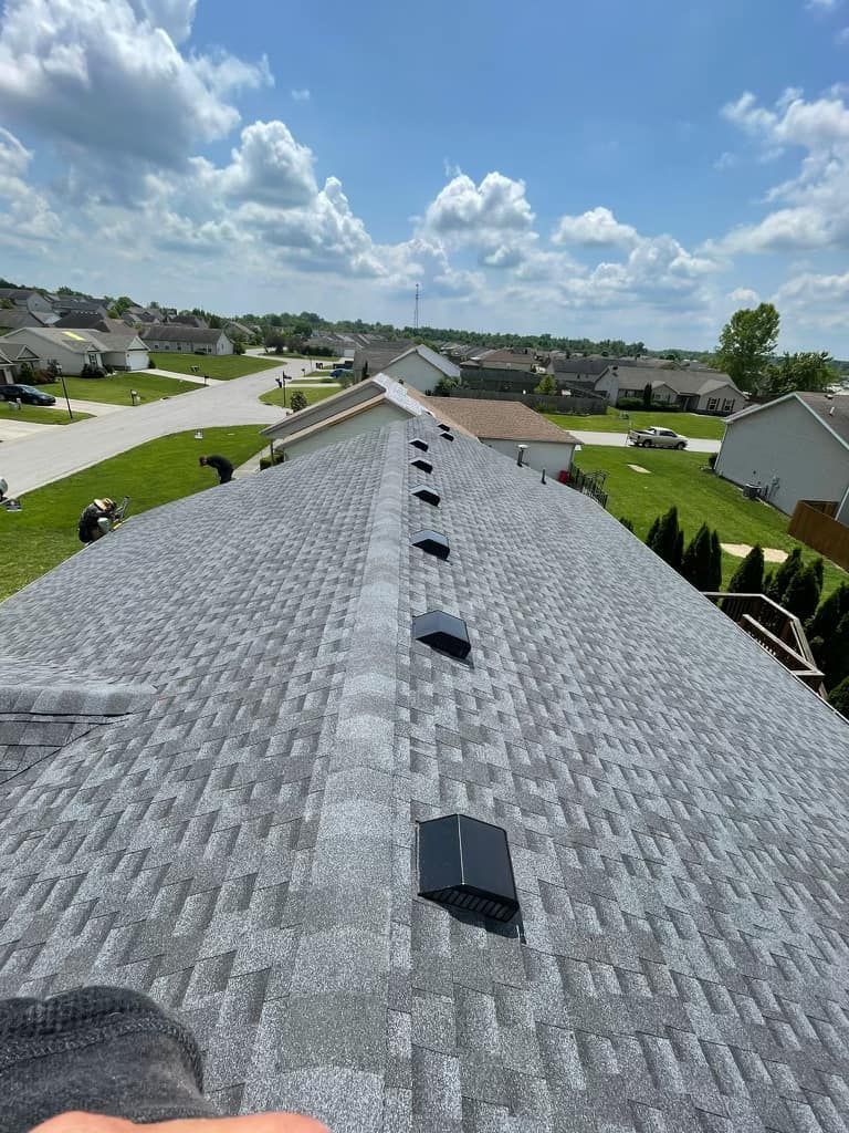 A high-angle view looking down the peak of a gray shingled residential roof with several black attic vents installed.