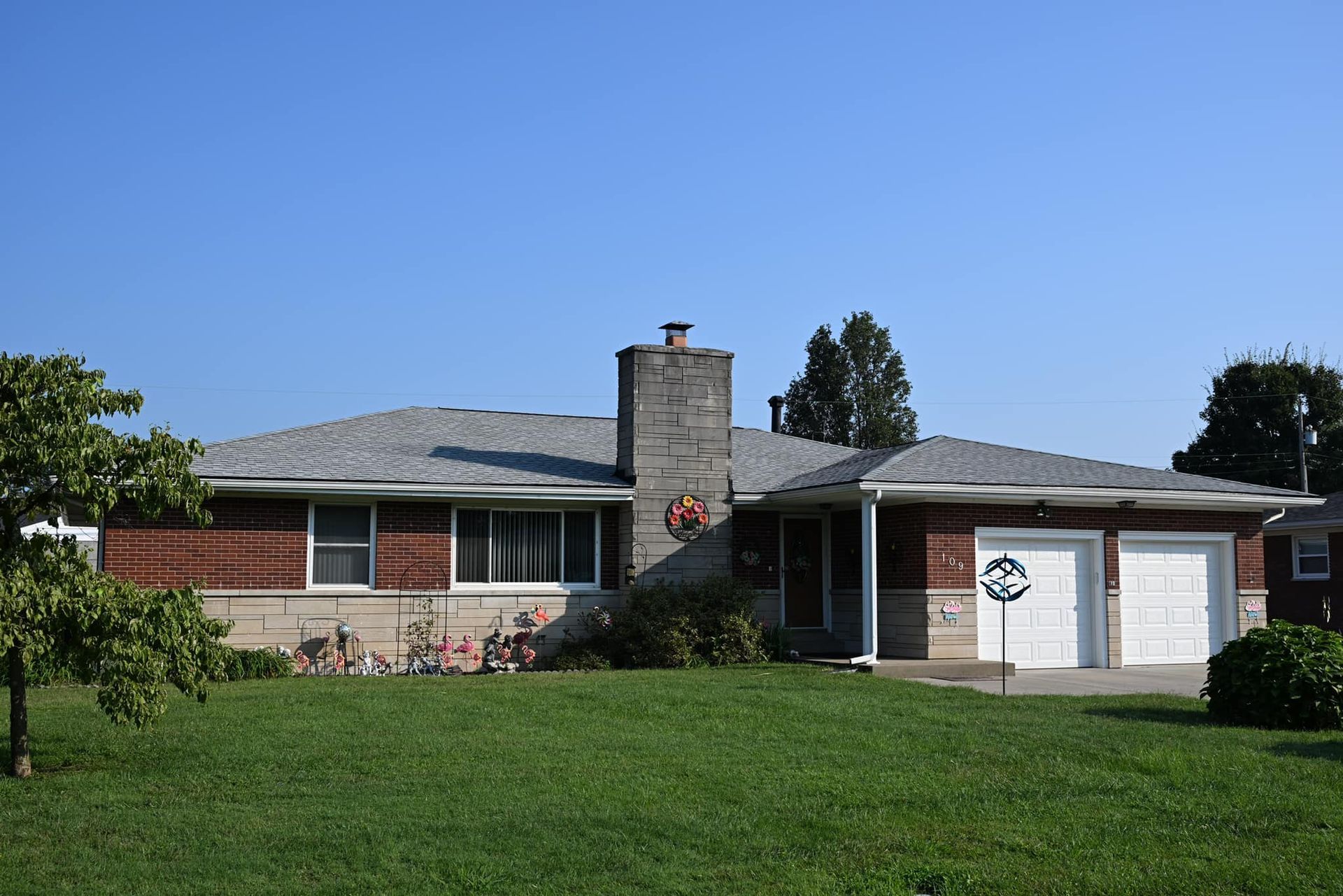 A single-story ranch-style home with a brick exterior, stone chimney, two-car garage, and a large front lawn.