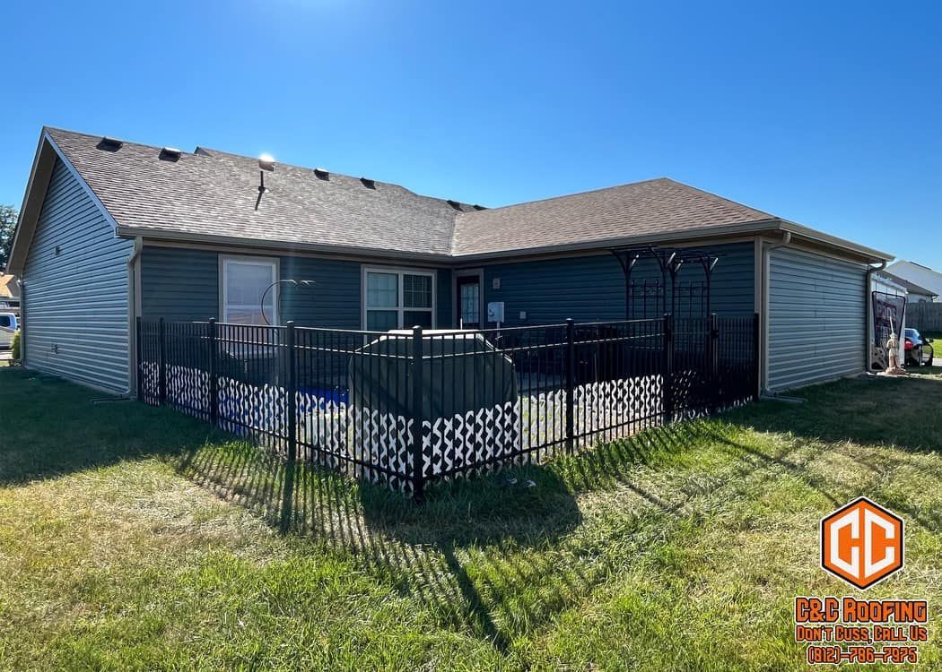 A single-story residential home with dark blue siding, a shingled roof, and a fenced-in patio area in the backyard.