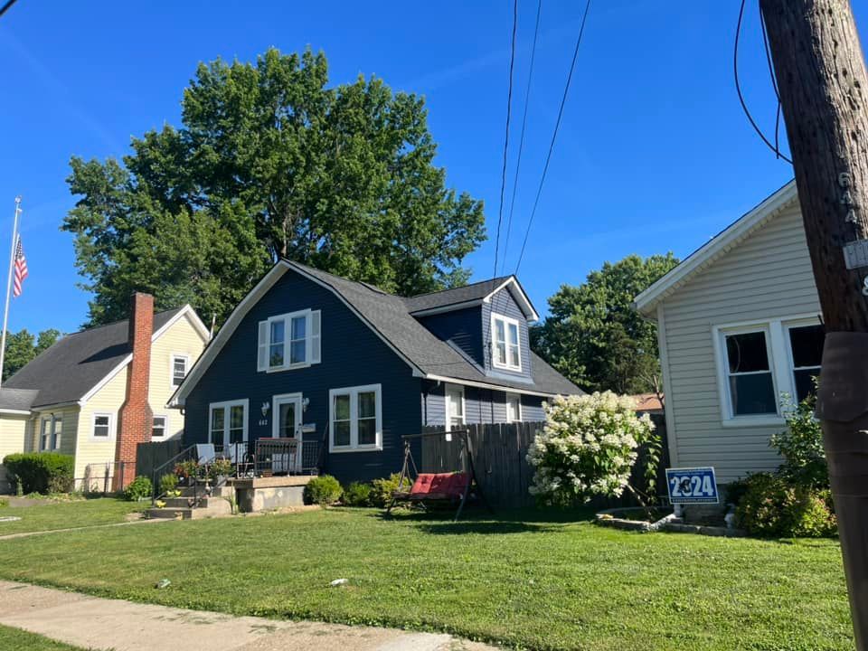 A blue, two-story house sits between a yellow house and a light-colored home under a clear blue sky on a sunny day.