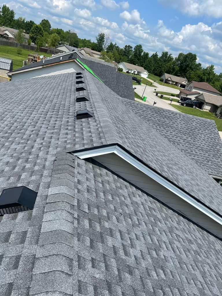 An overhead view of a gray shingled residential roof with multiple black roof vents and a large skylight.