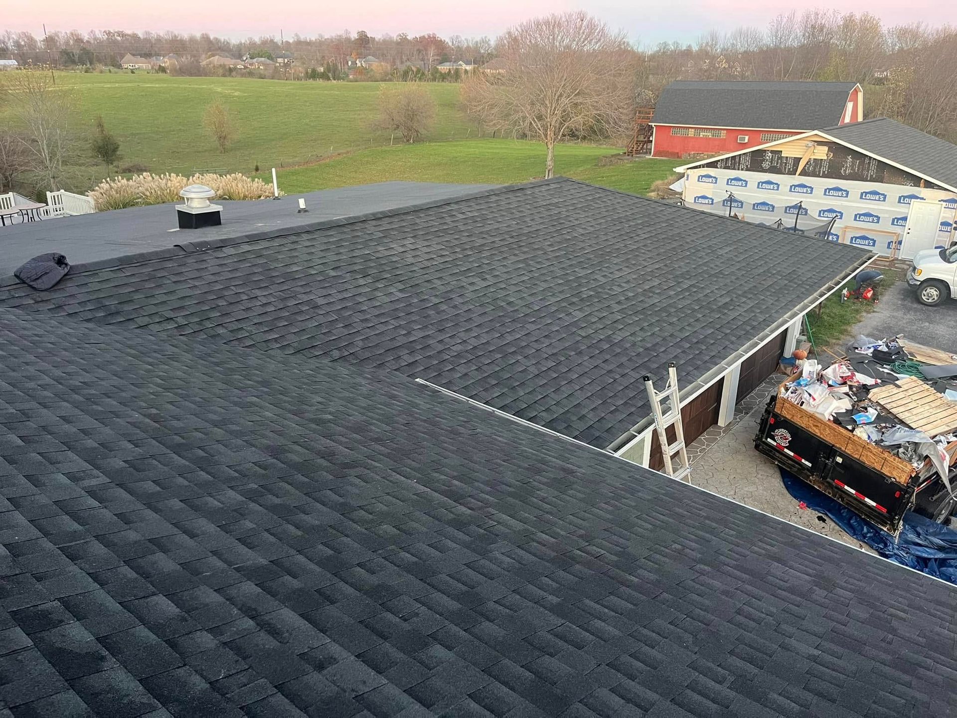 High-angle view of a newly shingled dark gray roof on a house and detached garage under a clear sky.
