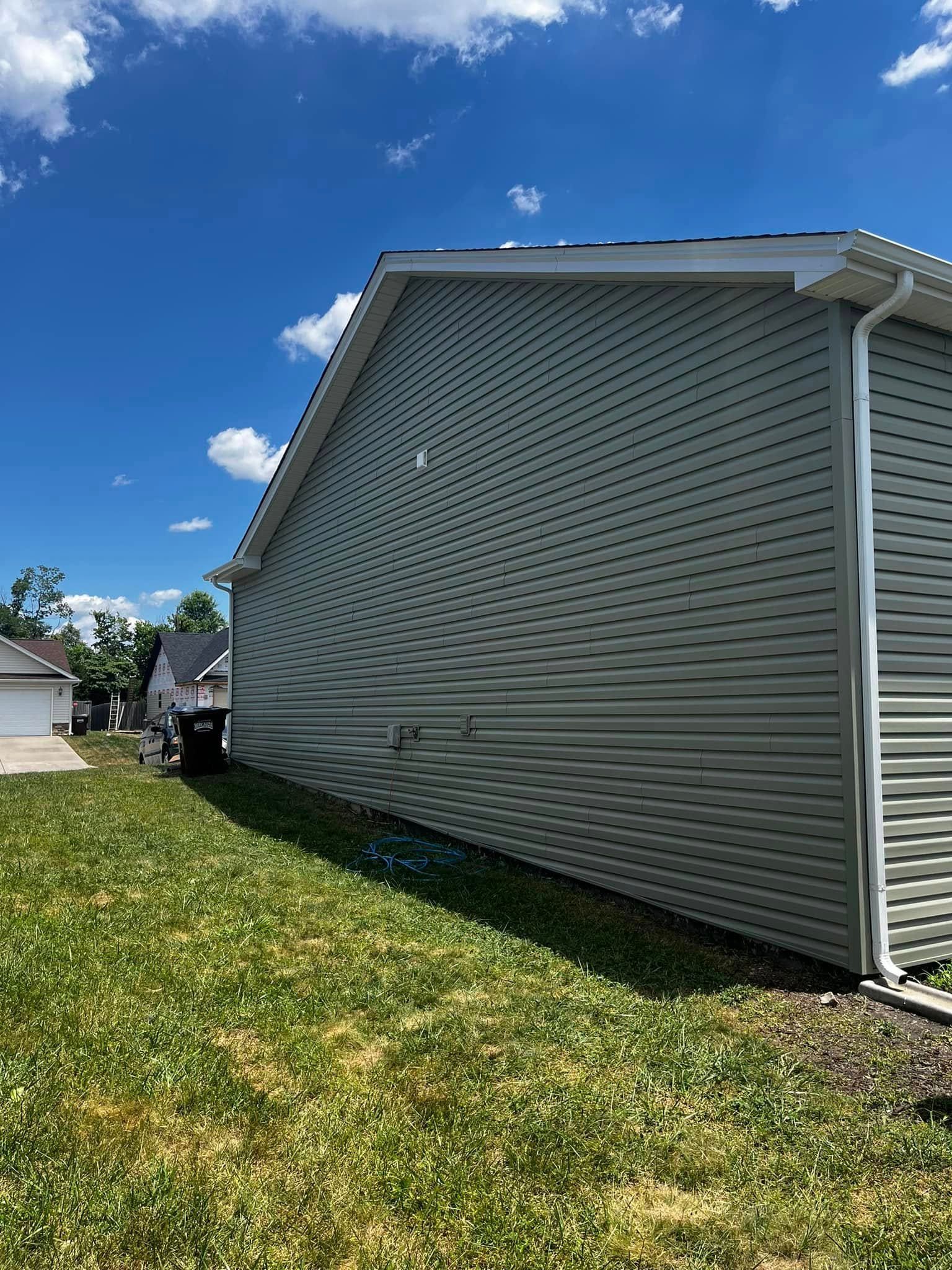 A view of the light-colored vinyl-sided exterior wall of a house under a bright blue sky with patchy clouds.