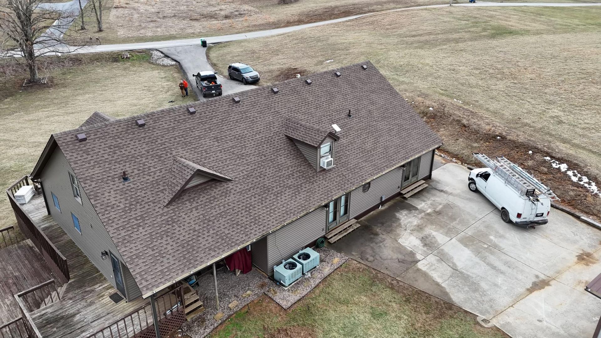 Aerial view of a house with a brown shingled roof, two dormers, and a driveway with a work van parked next to it.