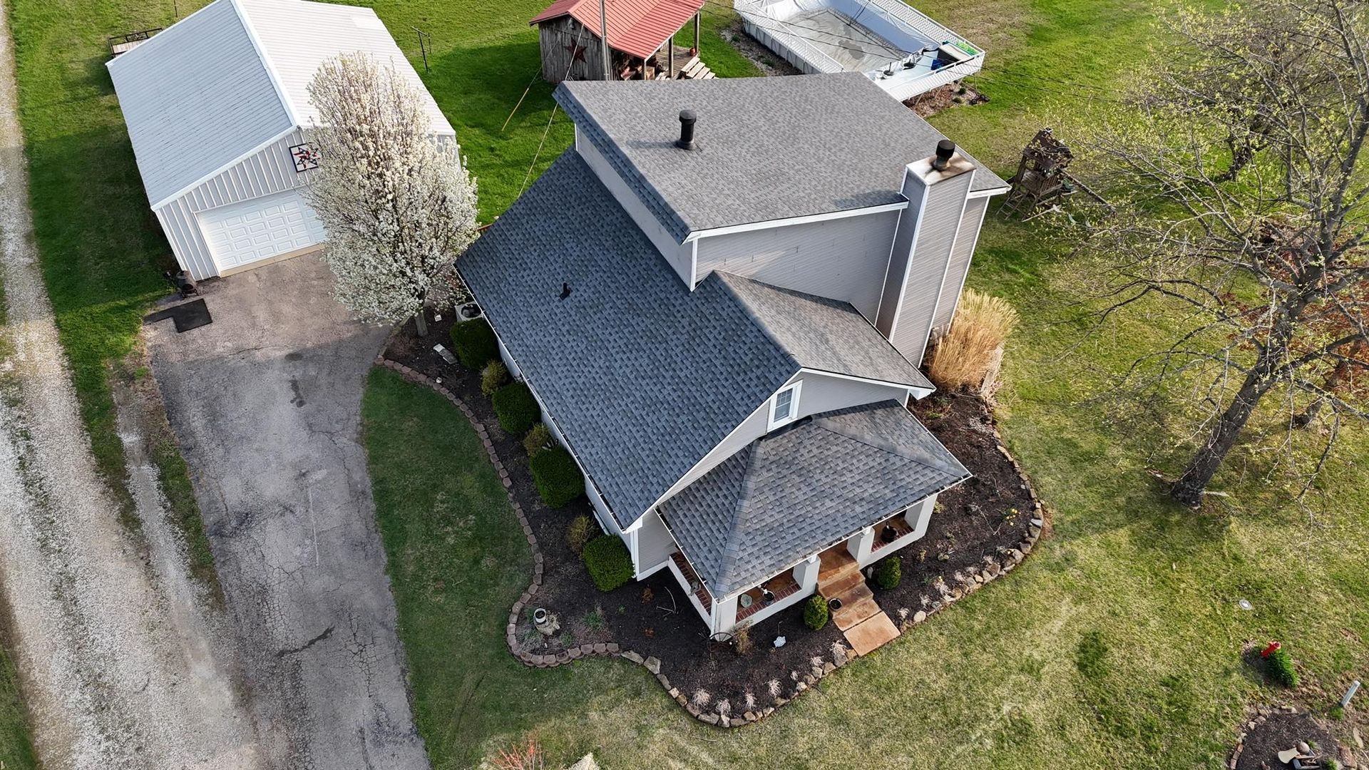 Aerial view of a two-story gray house with a shingled roof, an adjacent detached garage, and a lush green lawn.