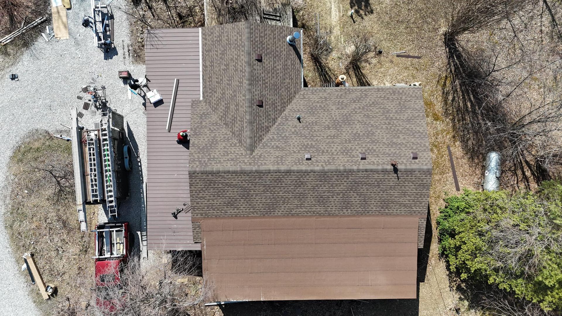 An aerial view of a house roof undergoing repairs, showing shingled and metal sections with a truck parked nearby.