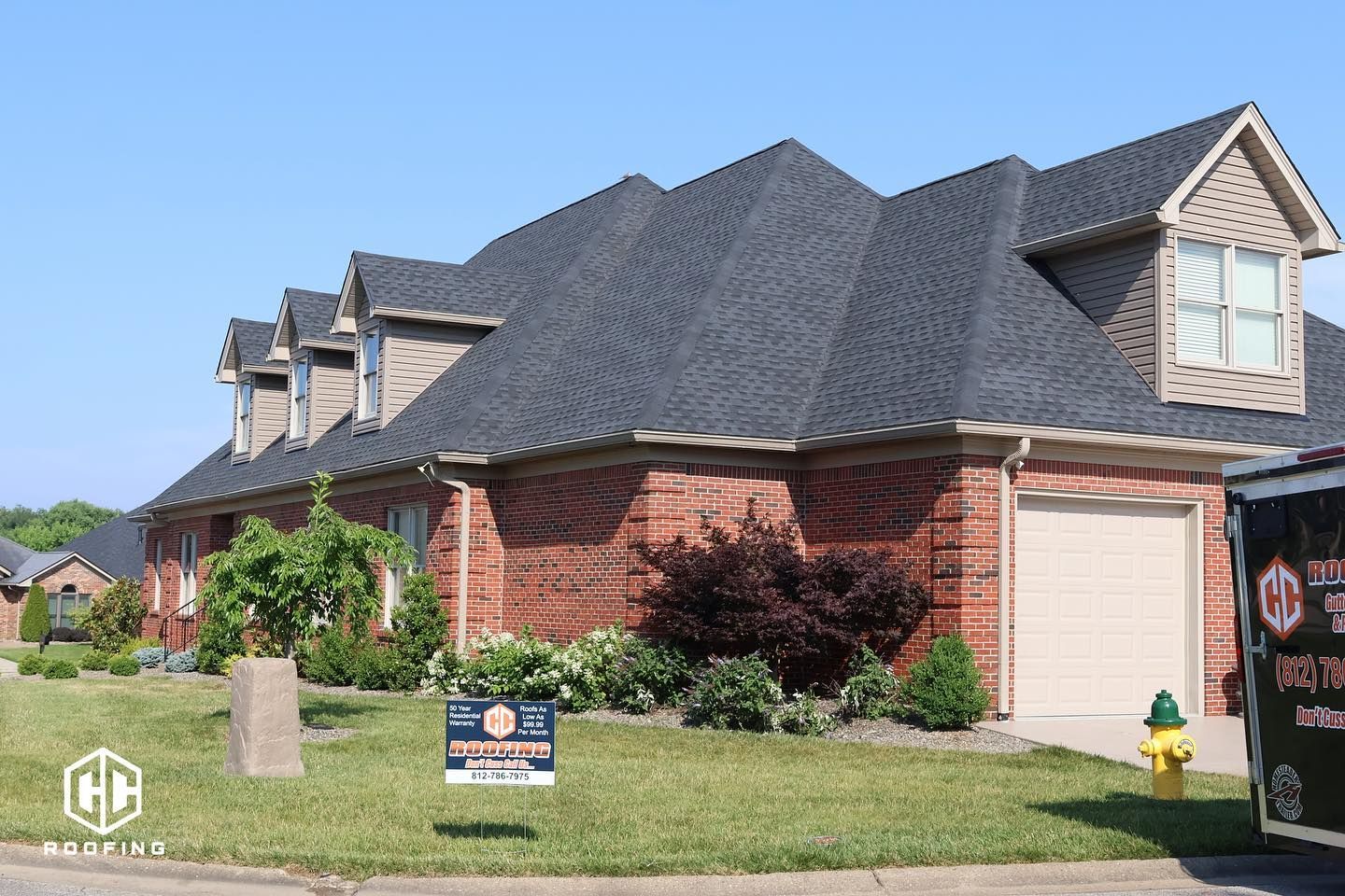 A large, one-story red brick house with multiple roof gables, a two-car garage, and a lawn sign, set under a blue sky.