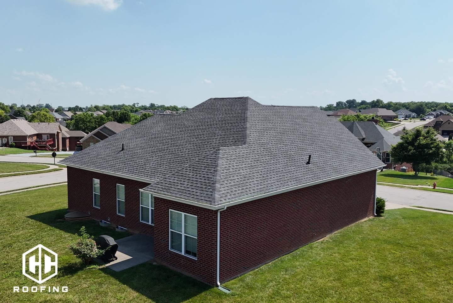 Aerial view of a red brick house with a dark grey shingled roof and a CC Roofing logo in the corner.
