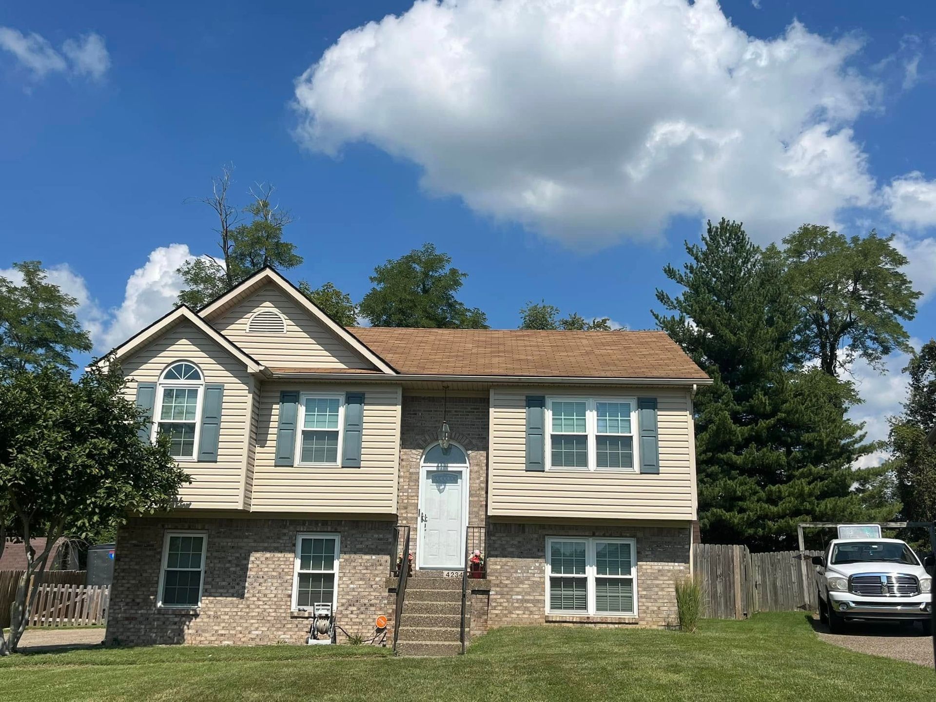 A two-story house with beige siding and brick on the bottom level, featuring a centered white door and a parked truck.
