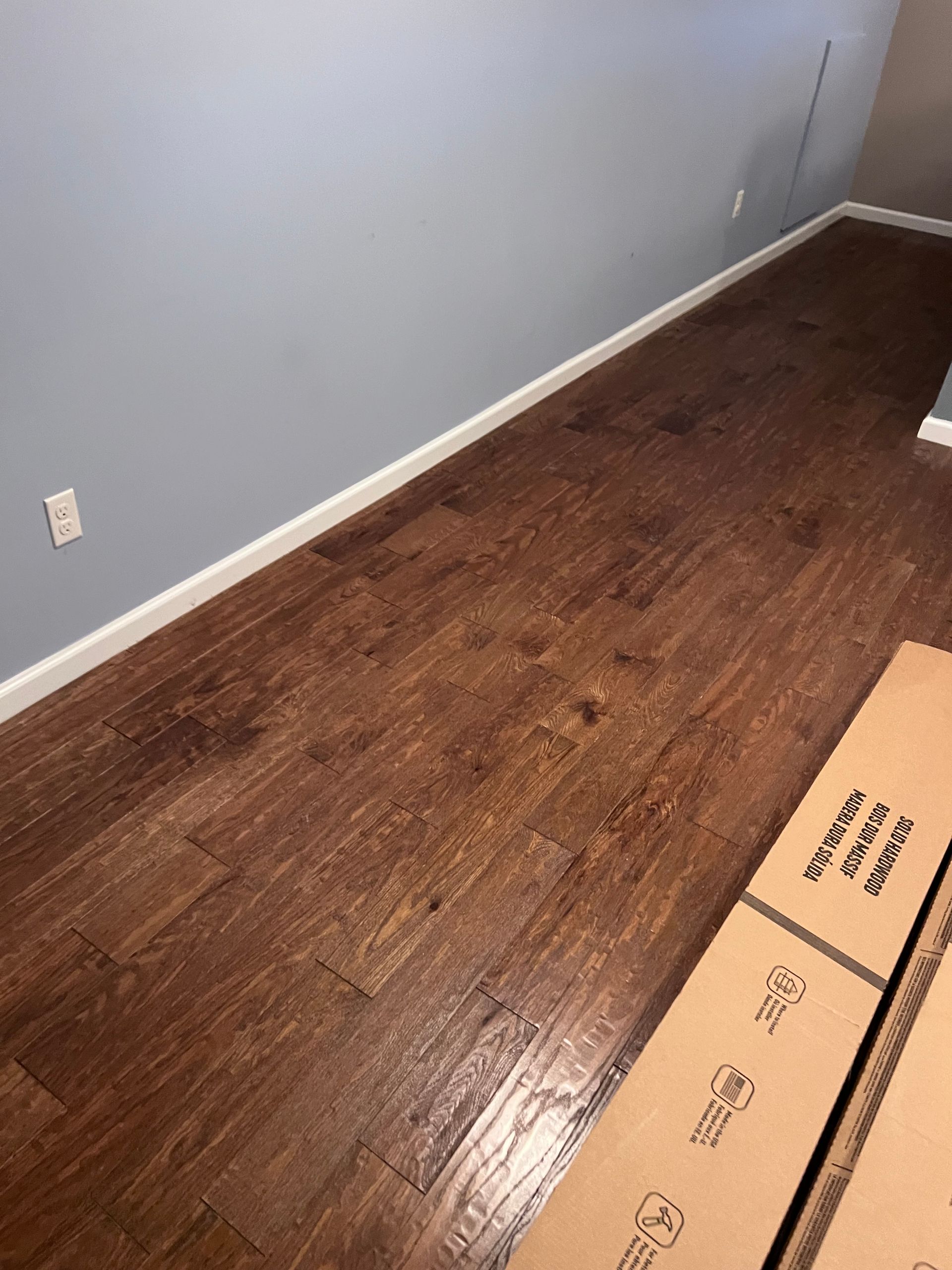 A living room with hardwood floors and a cardboard box on the floor.