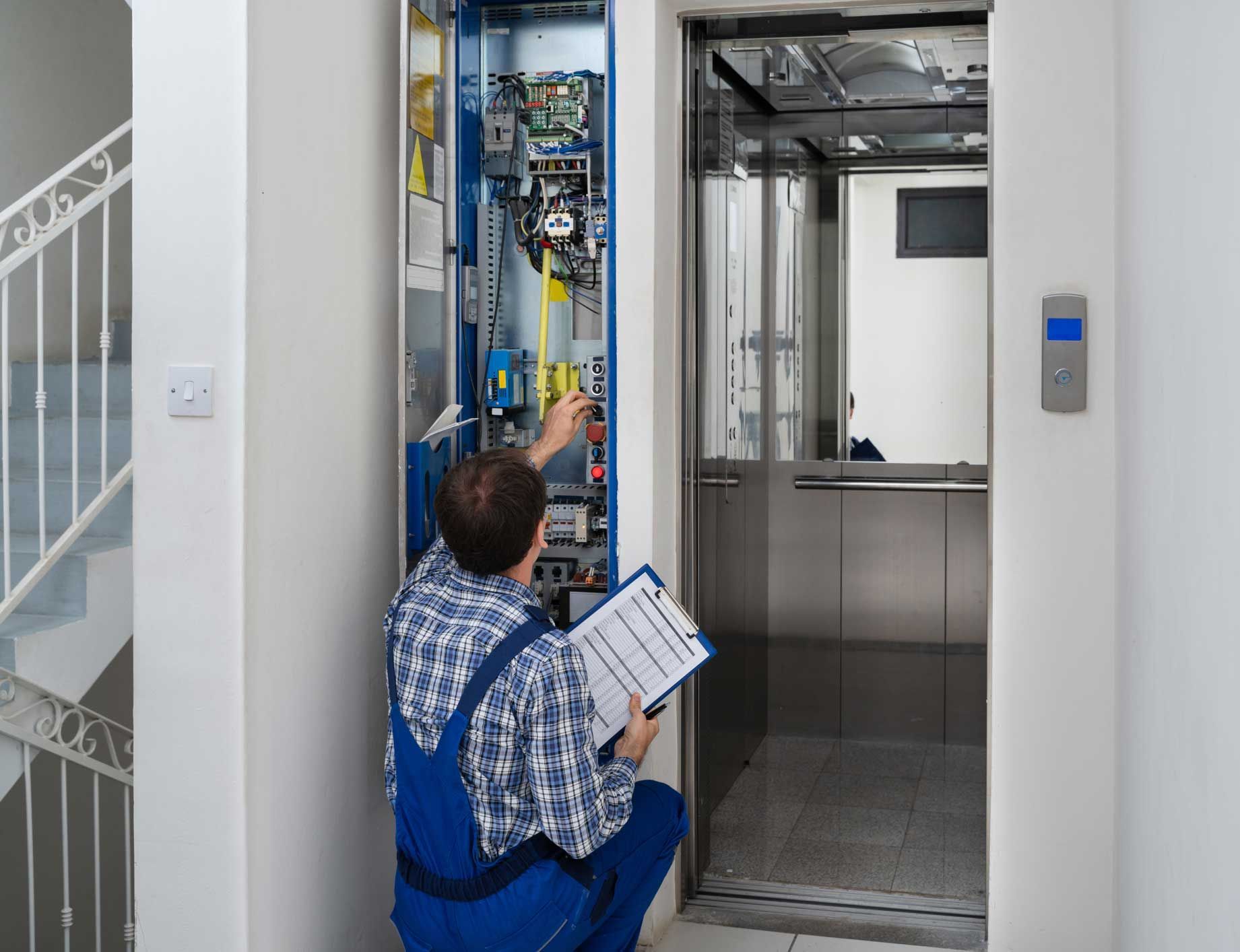 Technician inspecting elevator control panel, holding a clipboard, near elevator car.