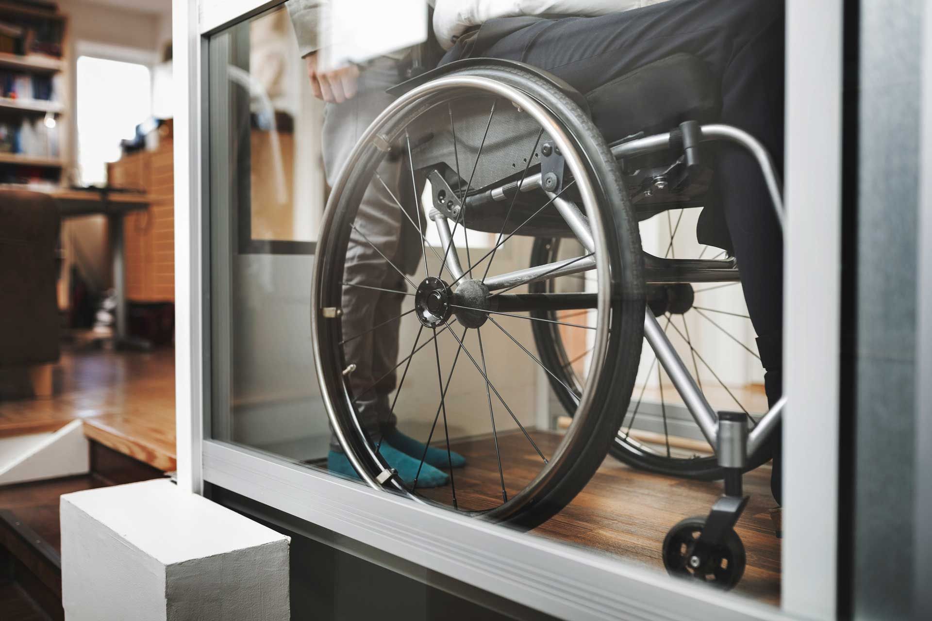 Person in a wheelchair indoors, low angle, focused on the wheel.