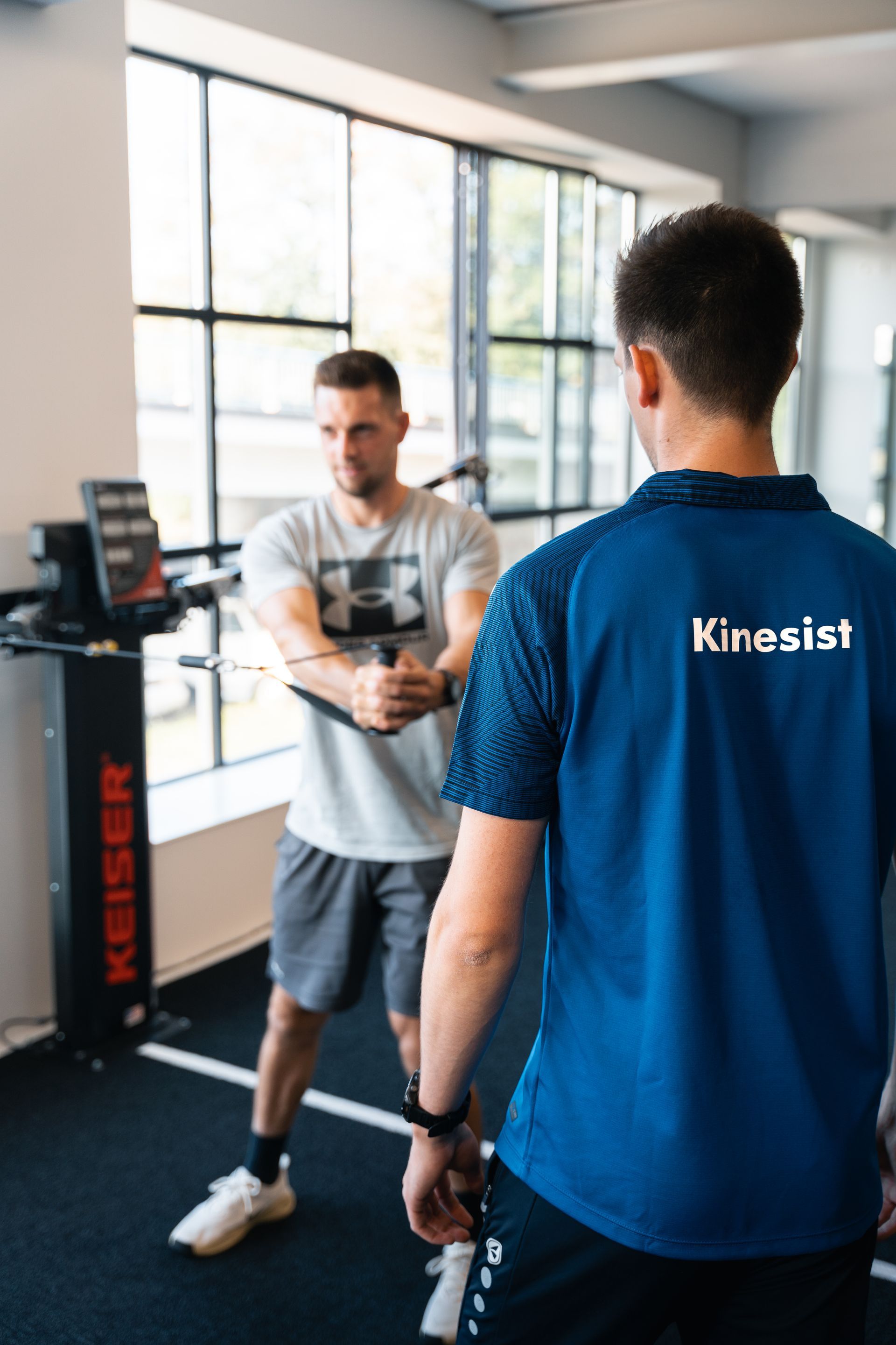 Fabian, kinesist bij Fysicure Mol, begeleidt een patiënt bij oefentherapie.