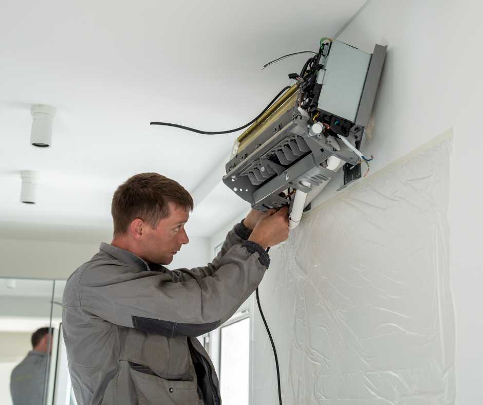 A man is working on an air conditioner on a wall.
