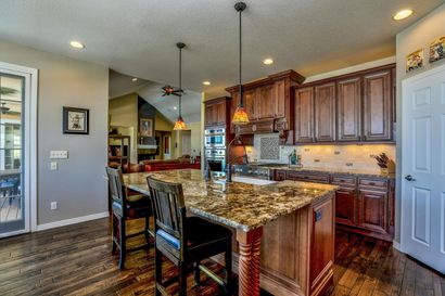 A kitchen with white cabinets , wooden floors , stainless steel appliances and a large island with chairs.