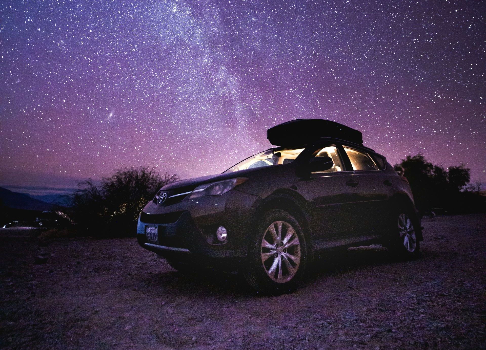A car with a roof rack on top of it is parked under a starry sky.