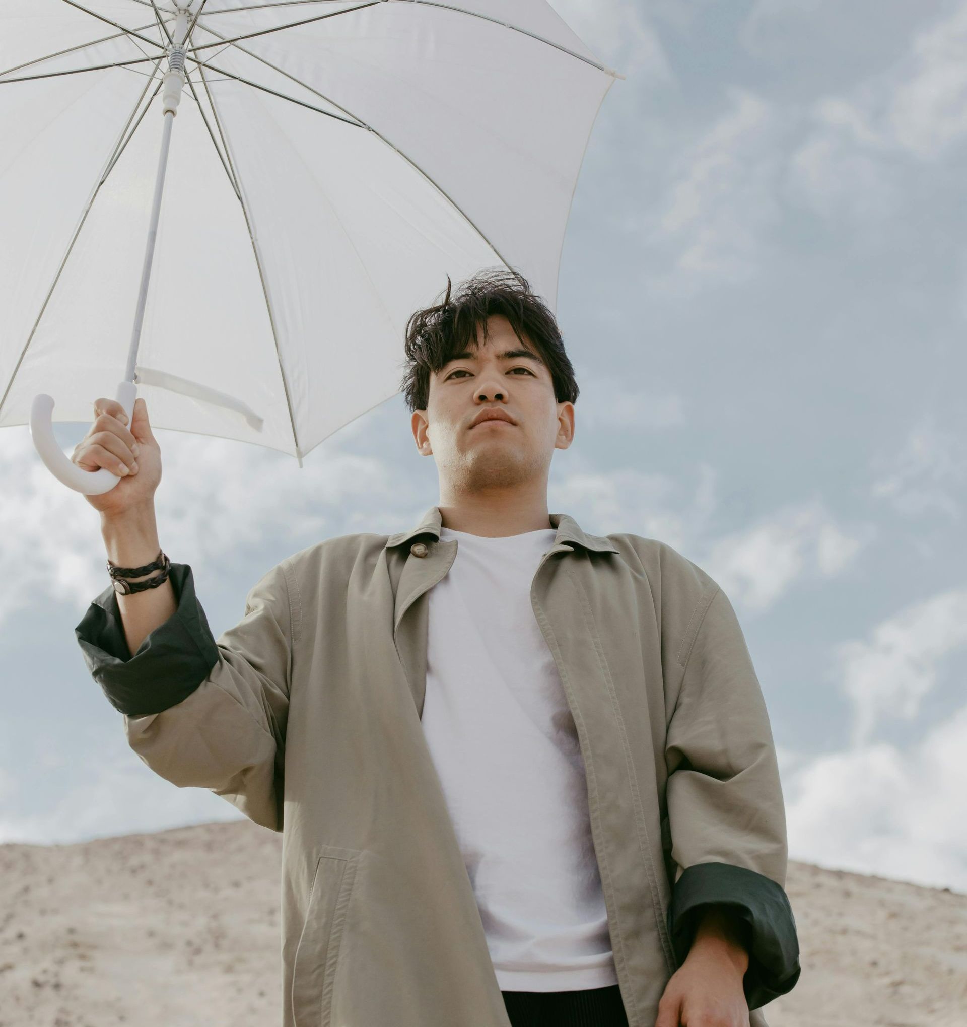 A man in a tan jacket is holding a white umbrella